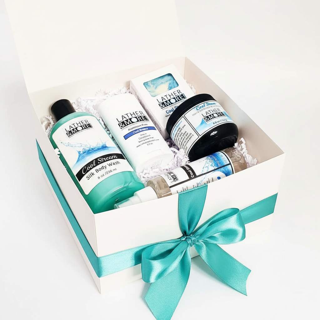 A boxed bath and body gift set from Lather and More, featuring a white box with a teal ribbon bow, filled with skincare products including a Cool Steam Silk Body Wash bottle, a deodorant tube, a body butter jar, and a small dry body oil bottle, all arranged on white tissue paper.