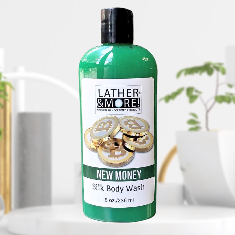 New Money Silk Body Wash with branding logo and product name with images of a bitcoin on the front label. Product is green liquid in a clear bottle with a black top on a white background with plants in the background.