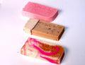A collection of various colored soap bars with branding labels on them, arranged in rows on a white surface.