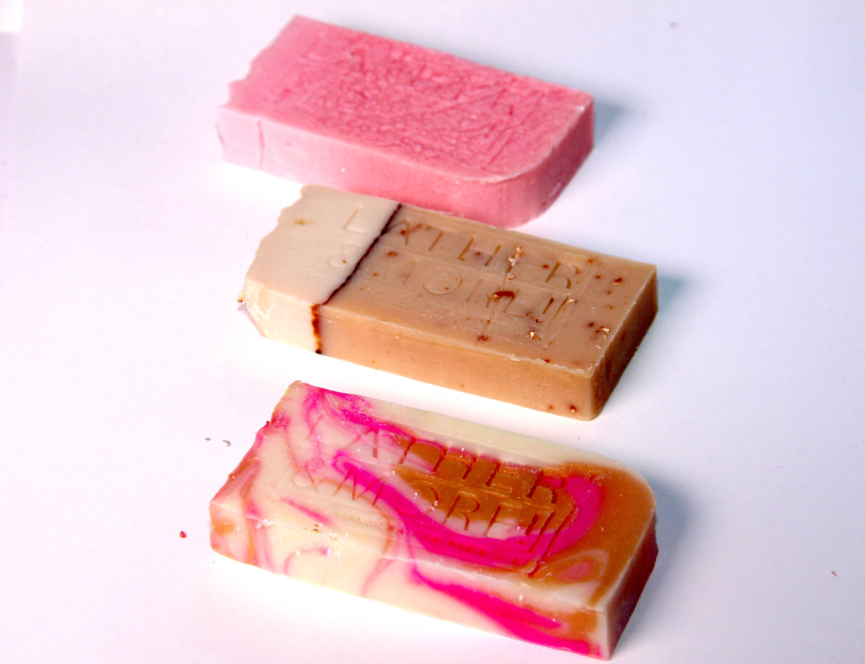A collection of various colored soap bars with branding labels on them, arranged in rows on a white surface.