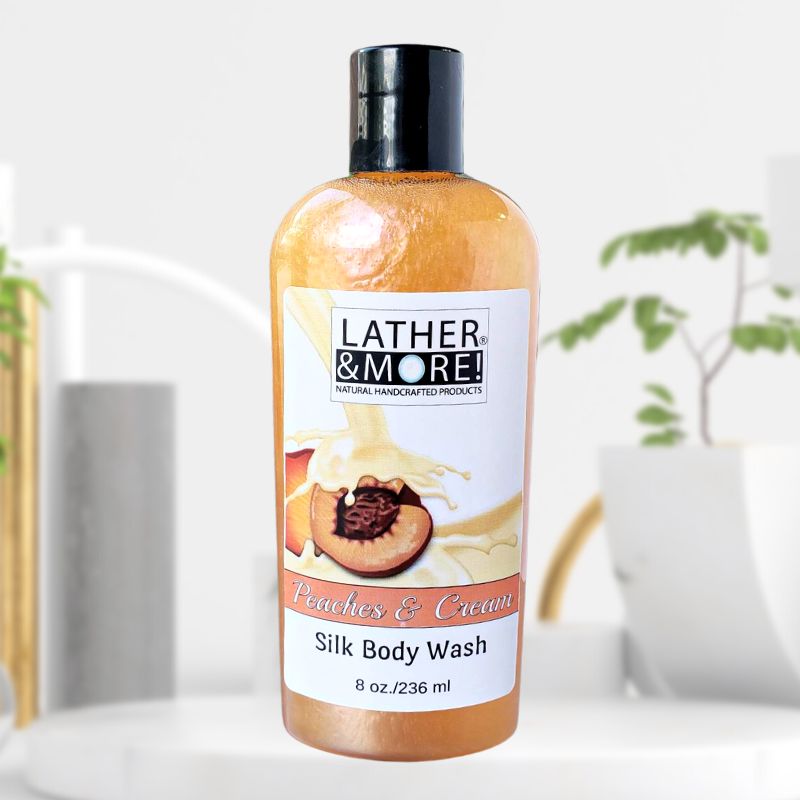 A bottle of Peaches and Cream Silk Body Wash by LATHER & MORE, with an image of a peach and cream on the label, displayed in a bathroom setting.