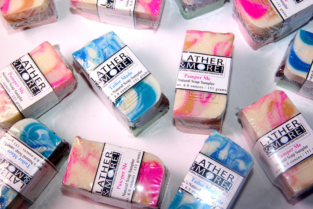 Multiple mini wrapped Lather More soap bars arranged on a white surface. The soaps are shown in various marbled colors including pink, blue, yellow, and cream, with Lather More branding clearly visible on the paper labels.