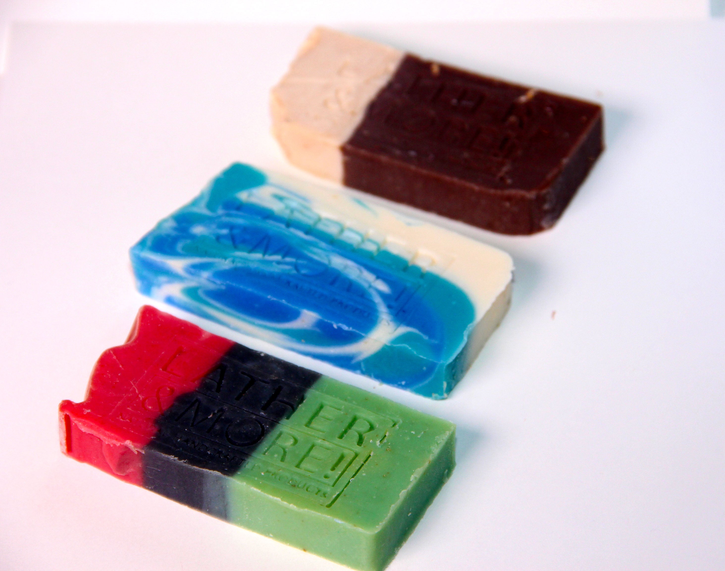A collection of various colored soap bars with branding labels on them, arranged in rows on a white surface.