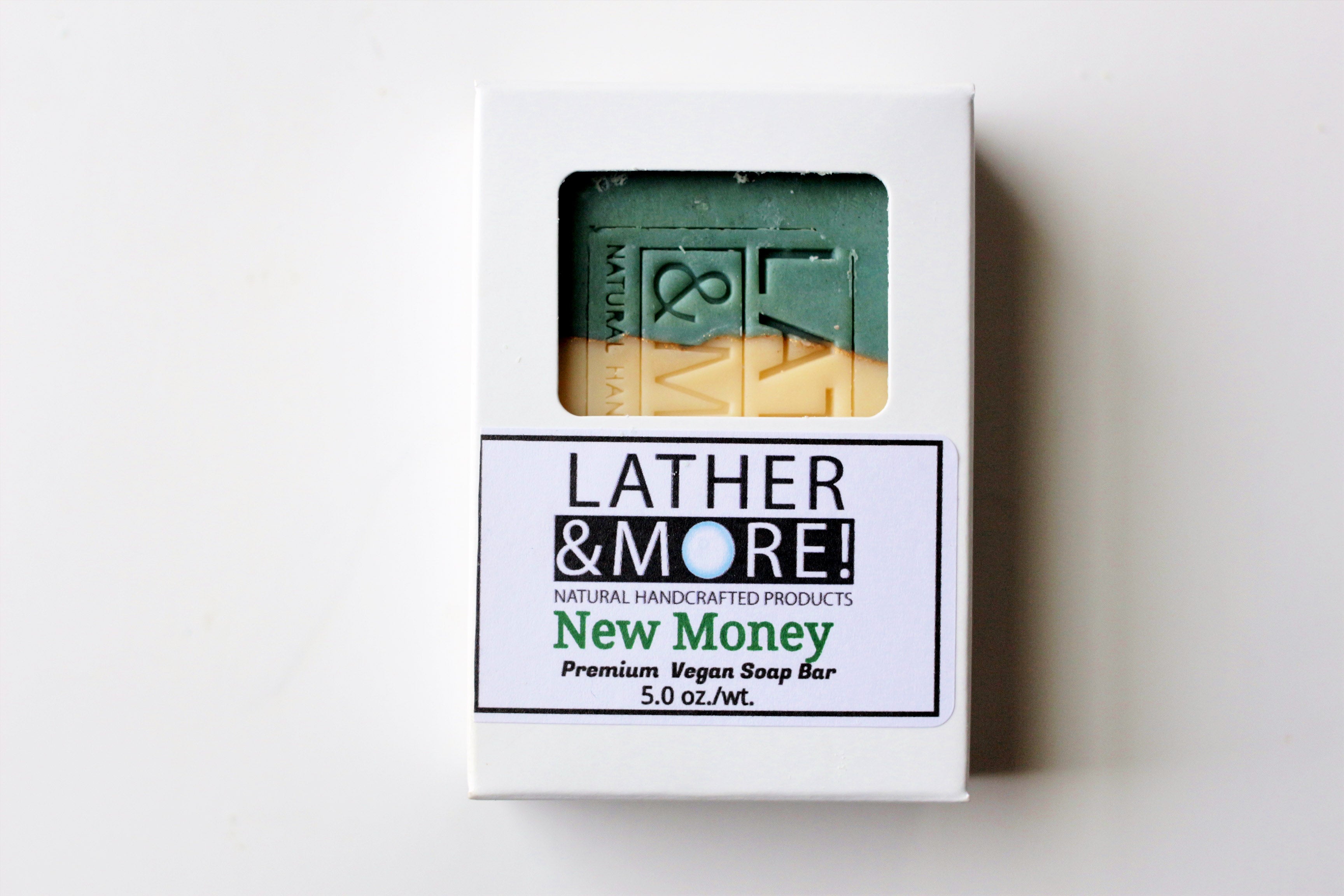 New Money Men's Soap - green top, cream bottom, gold mica line separating the two colors. Soap is incased in a white carboard soap box with a window that shows the soap design. Soap is standing up against a white background.